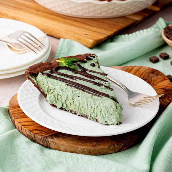 A slice of chocolate mint cheesecake with a chocolate crust, mint filling, and chocolate drizzle.