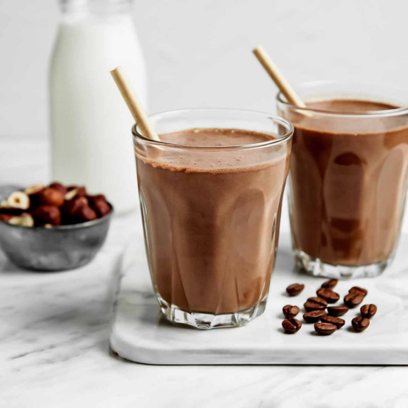 Two glasses of chocolate protein shake on a white marble surface