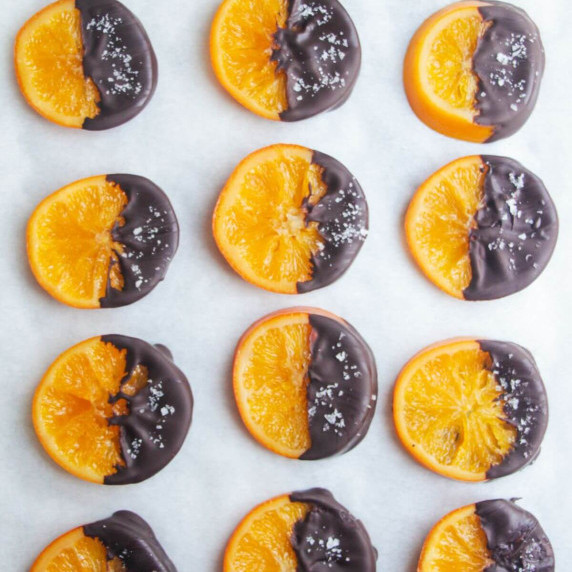 Dark chocolate dipped oranges slices on a baking paper lined background.