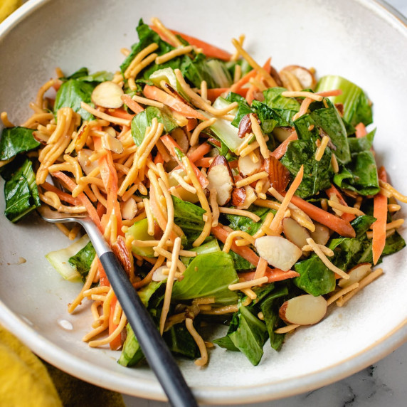 Bok Choy, carrots, slivered almonds and crispy chow mein noodles on a white plate with a fork