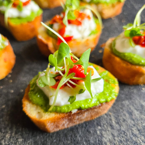 Golden toasty topped with green pesto, white cottage cheese, red peppers, and green microgreens.