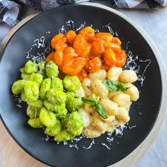 Red sauced gnocchi, green pesto gnocchi, and creamy white sauce gnocchi on a black plate