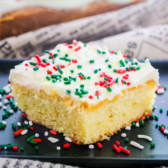 A slice of yellow cake topped with cream cheese icing and christmas sprinkles
