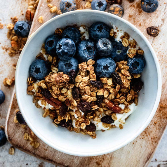 Cinnamon granola in a white bowl with fresh blueberries