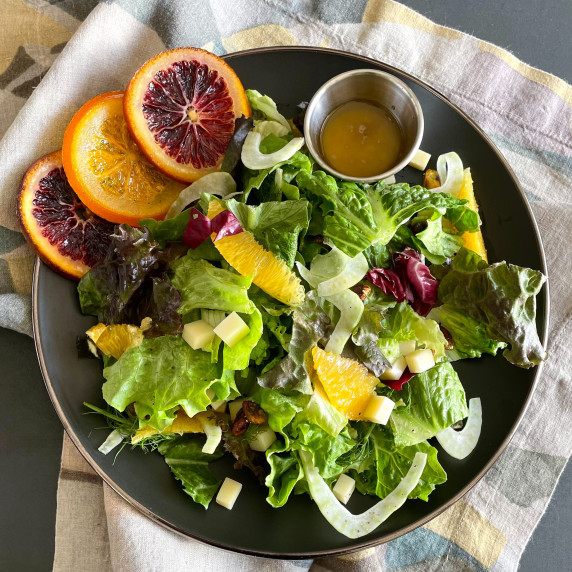 Fresh citrus salad with mixed greens, fennel, cheese in a bowl with blood orange vinaigrette.