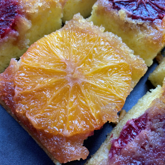 Slice of yellow cake topped with an orange slice on a black platter.