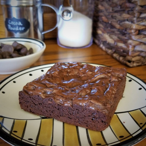 Single brownie on a plate with ingredients in the background.