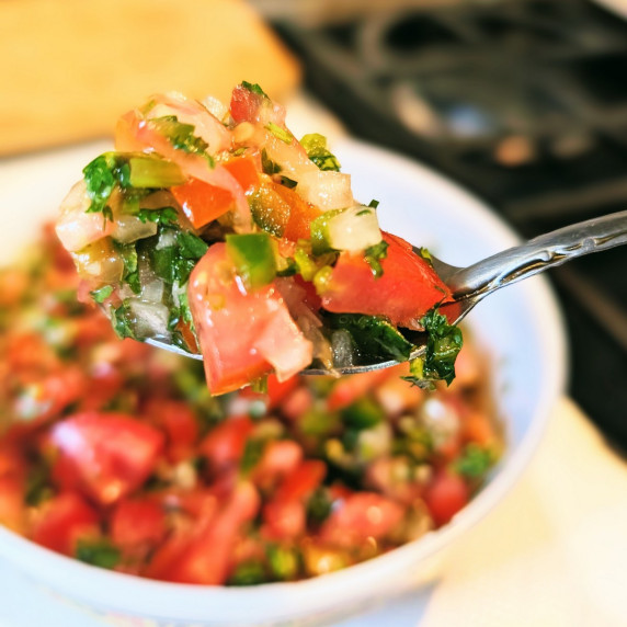 Pico de gallo salsa on a spoon with more in a bowl in the background