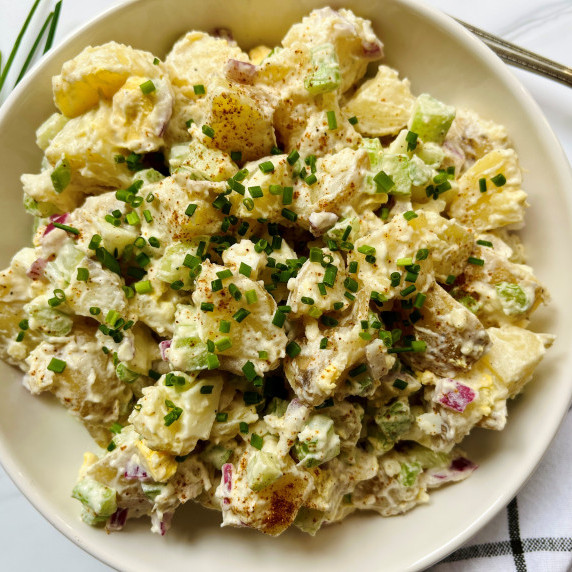 Creamy potato salad topped with chives in a white bowl.