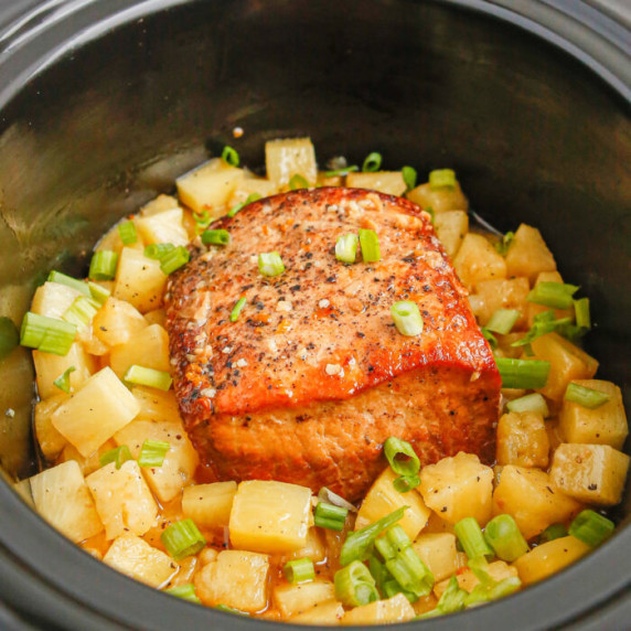 Close up view inside a slow cooker with cooked pork loin and pineapple.