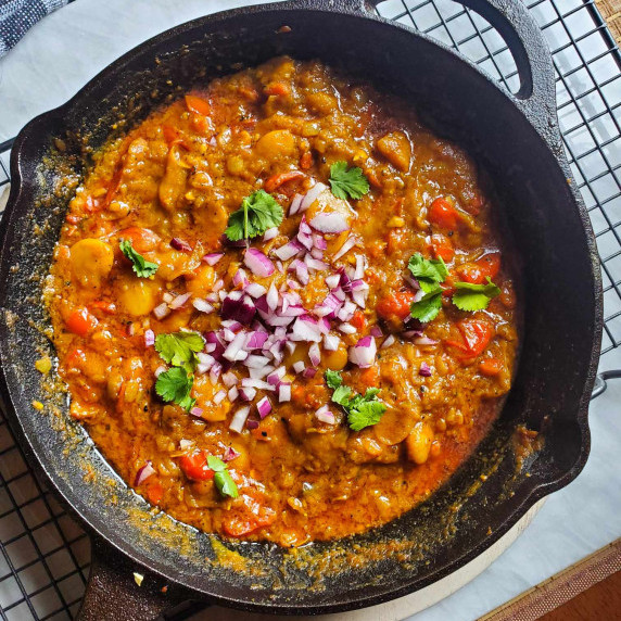 A skillet full of rich butter beans topped with red onions and green cilantro.