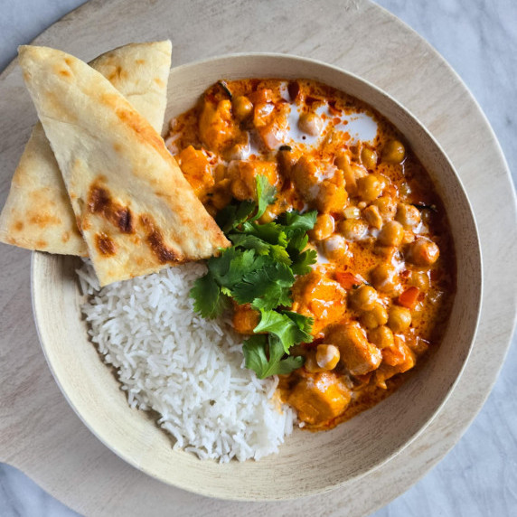 A bowl of bright, orangey red curry with white basmati rice and green cilantro.