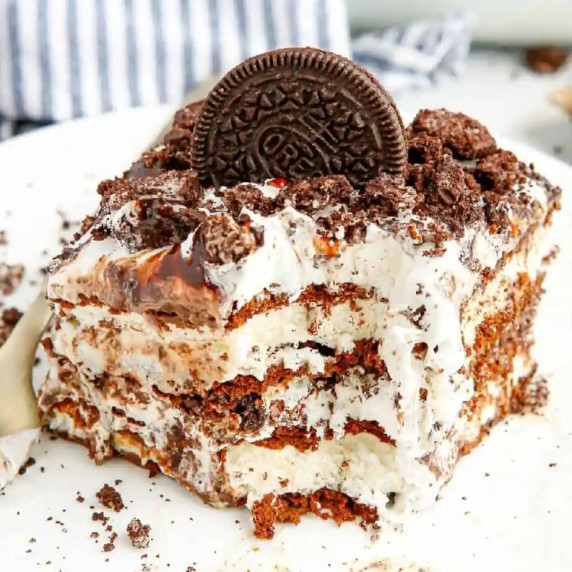 Slice of cookies and cream ice cream cake with a bite missing at the corner showing the layers.