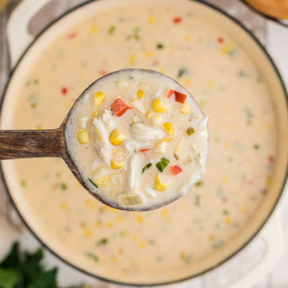 a spoon full of corn and crab bisque above a pot of the soup