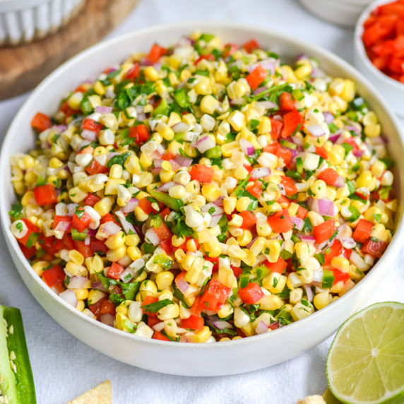 A bowl of corn salsa that has corn kernels, bell pepper, red onion and cilantro.