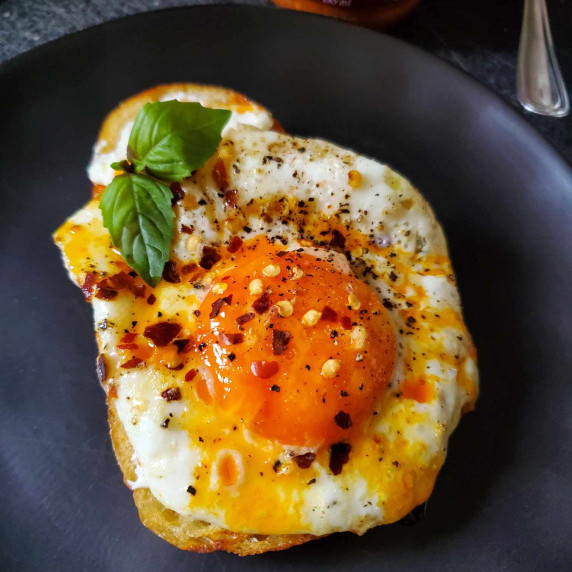 A perfectly fried egg on top of grilled toast on a matte black plate.