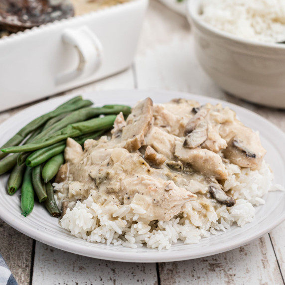 a plate full of rice with chicken in a gravy over the top with some green beans in the background