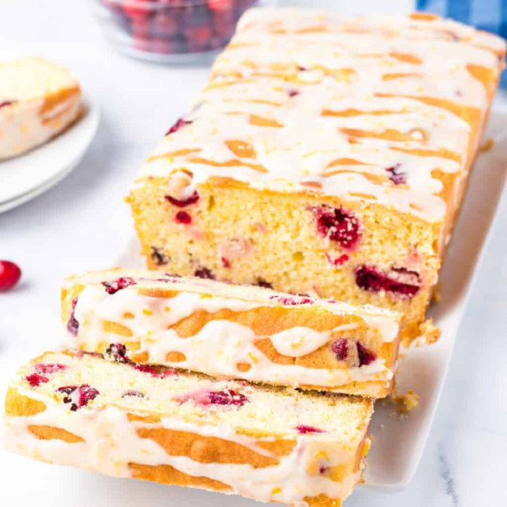 Sliced cranberry orange bread topped with glaze at an angle on a platter to see the sliced loaf.