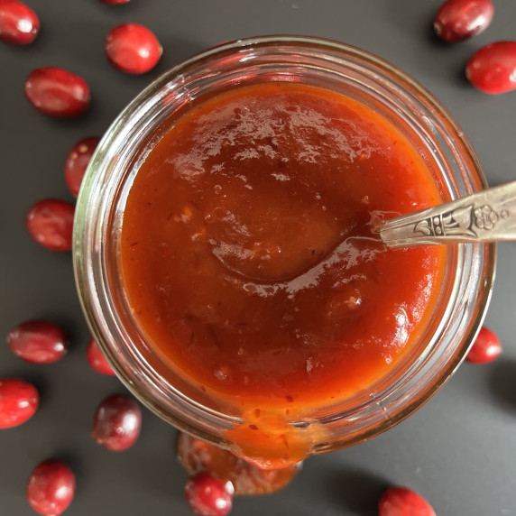 Cranberry barbeque sauce in a clear jar on a black countertop.