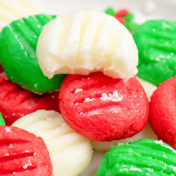 Close up of white, green and red cream cheese mints with the top mint missing a bite from the side.