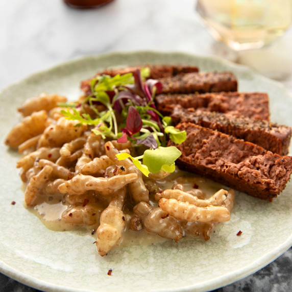 Creamed crosnes on a plate alongside sliced plant-based steak, topped with microgreens.