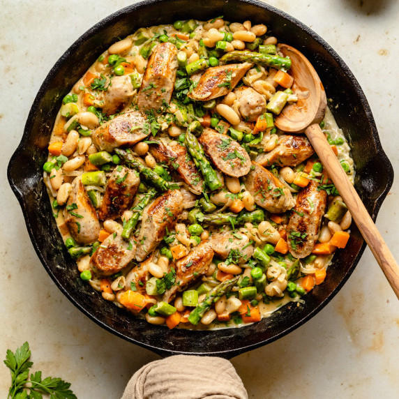 Cast iron skillet with chicken sausages and veggies in a creamy sauce and spoon to serve.