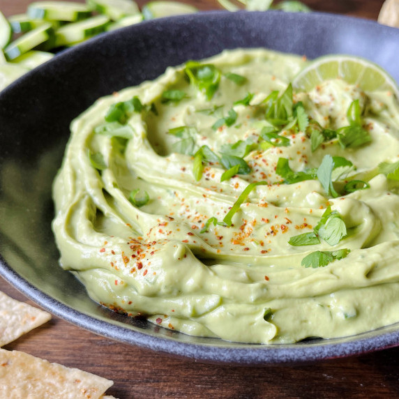 Avocado dip garnished with cilantro, green onion and slice of lime in a gray bowl.