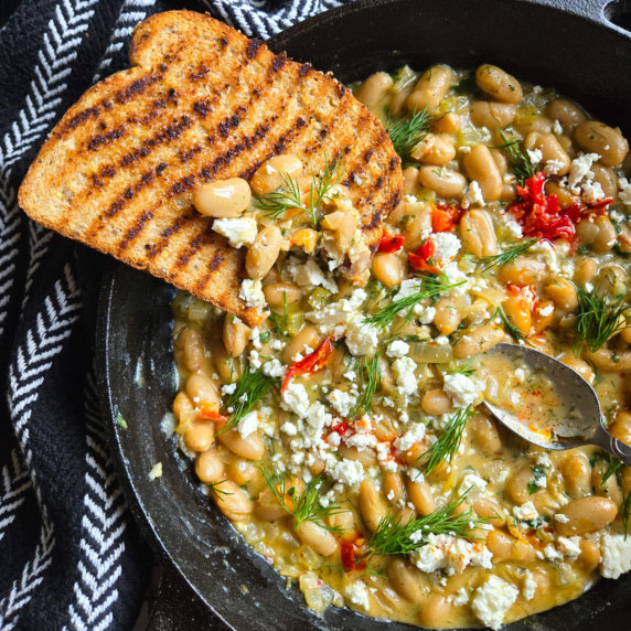 Creamy beans with a golden, grilled piece of toast, white feta, red pepperoncini, and green dill.