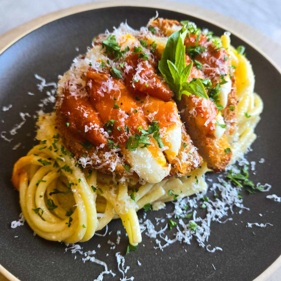 A golden nest of bucatini topped with plant-based chik'n smothered in mozzarella and red sauce