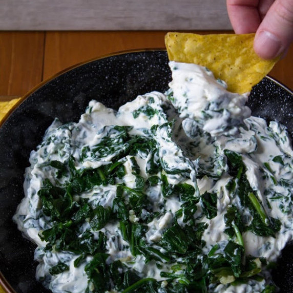 Creamy Garlic Spinach Dip in a black bowl with a chip being dipped