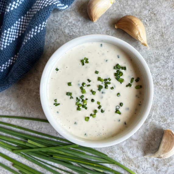 Creamy garlic dressing in a white bowl garnished with fresh minced chives.