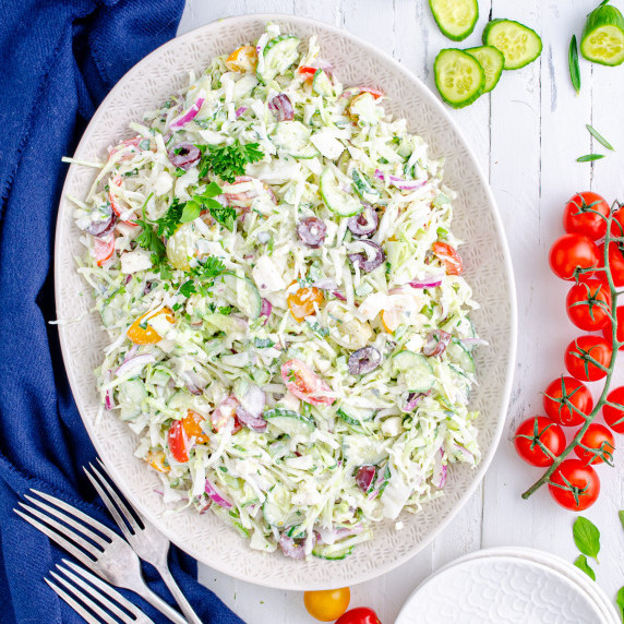 Creamy Greek Coleslaw on an oval plate surrounded by a blue napkin and fresh produce