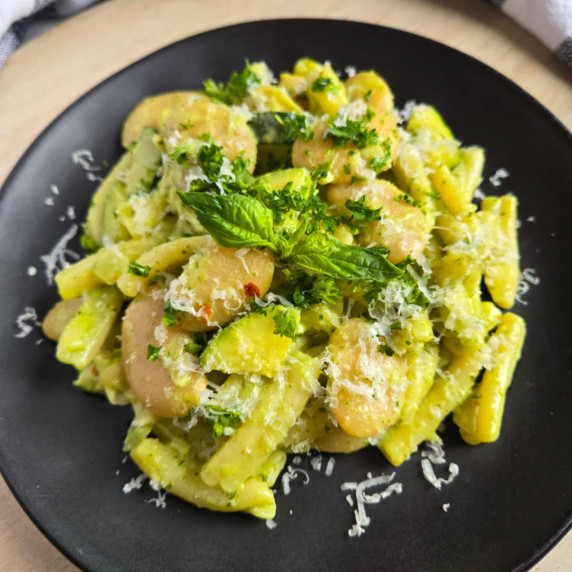 A bright green pasta on a black plate garnished with fresh green herbs