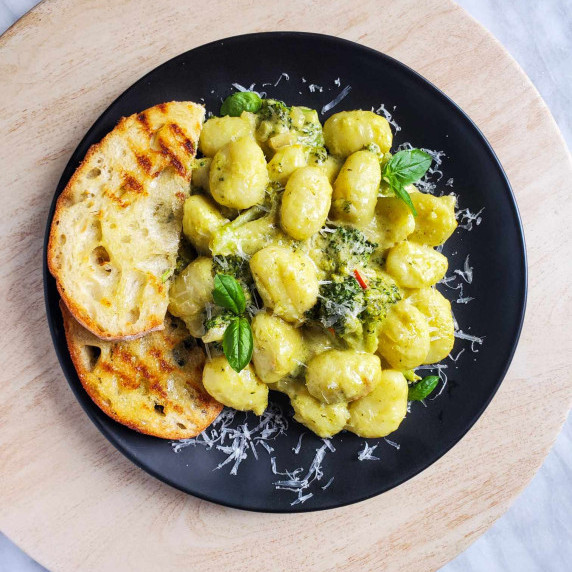 Golden brown toast and creamy, green pesto gnocchi on a black plate against a wooden board.