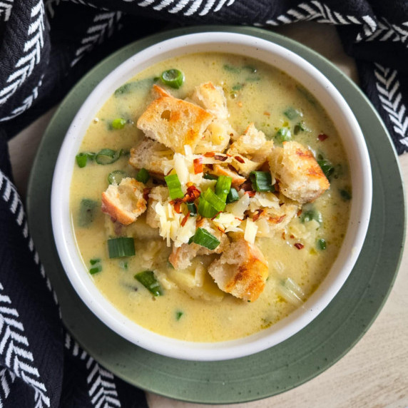 A bowl of creamy potato soup garnished with croutons & greens against a green plate and black towel.