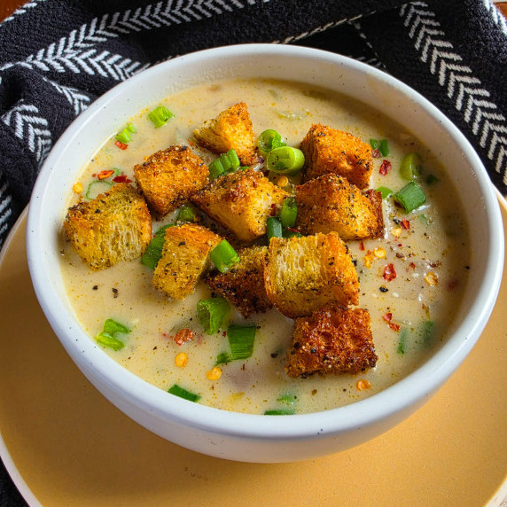 Creamy bowl of potato soup with golden croutons against a black towel.