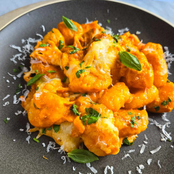 A plate of gnocchi sauced in an orange pepper sauce and finished with green herbs