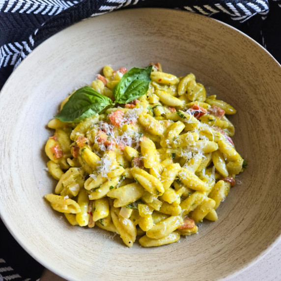 A wooden bowl full of green hued cavatelli with a black patterned towel in the background.