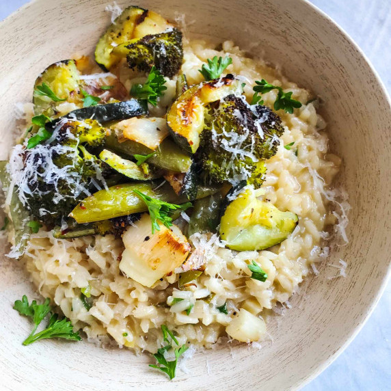 A bowl of risotto topped with an assortment of roasted green vegetables.