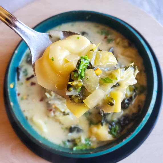 a spoonful of tortellini soup with flecks of green herbs and red pepper flakes