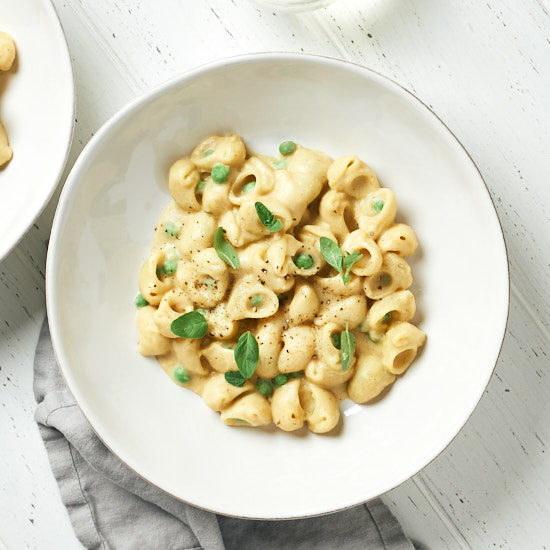 Creamy pasta with peas in a white bowl on a white wood counter.
