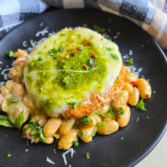 Creamy beans topped with a golden patty & gorgeous green pesto on a black plate.