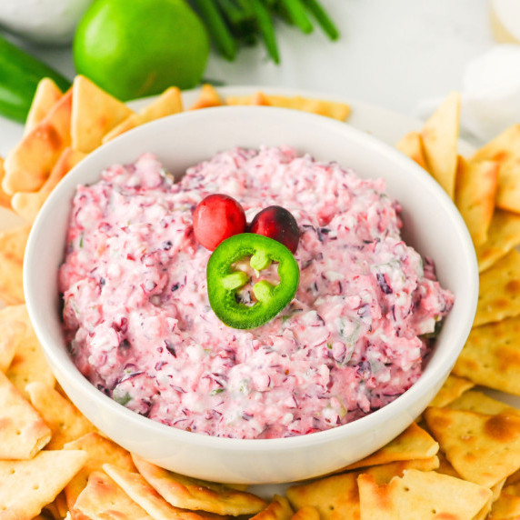 Creamy cranberry jalapeño cream cheese dip in a white bowl, topped with cranberries and a jalapeño s