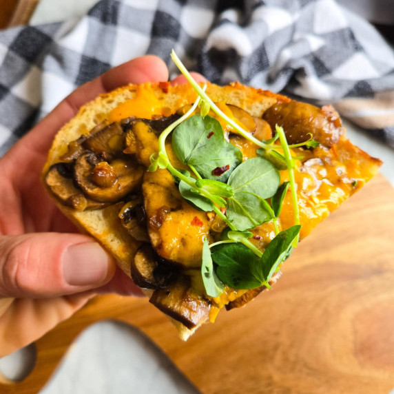 Golden toast with brown mushrooms, bright orange cheddar, and green pea shoots.