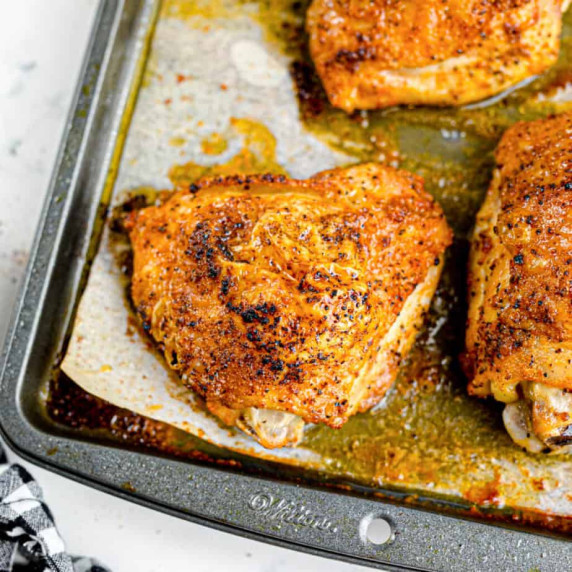 Golden brown baked chicken thighs sitting in juices on the pan close up.