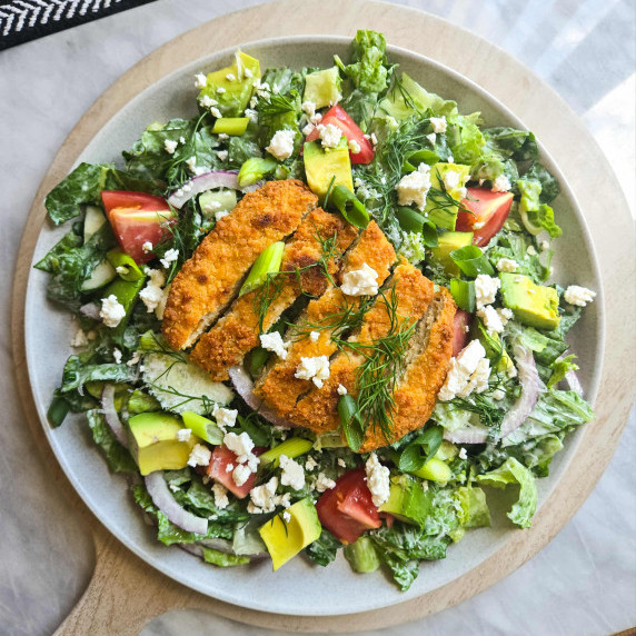 A colourful salad topped with golden, plant-based chik'n on a white plate.