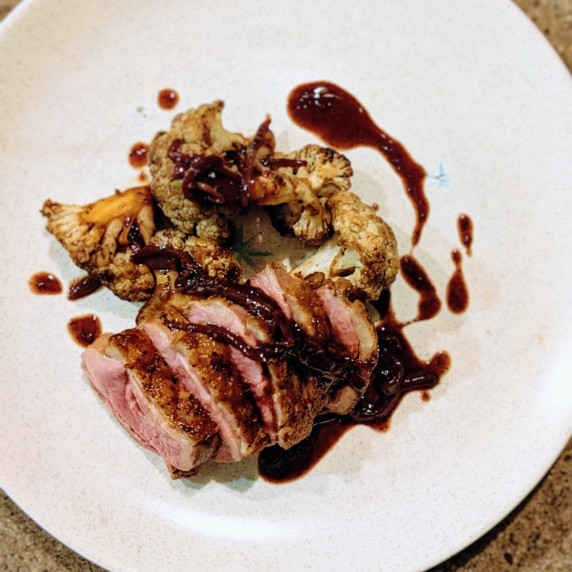 crispy duck breast with red wine pan sauce and grilled cauliflower on a white plate