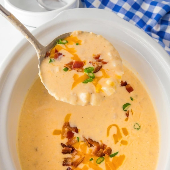 A ladle holding a scoop of creamy hash brown potato soup being scooped from a slow cooker.