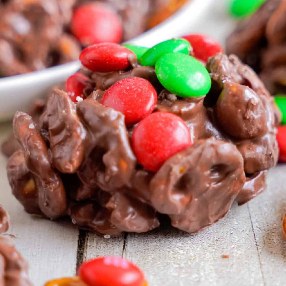 Close up of a chocolate cluster full of pretzels topped with green and red M&Ms on a counter.