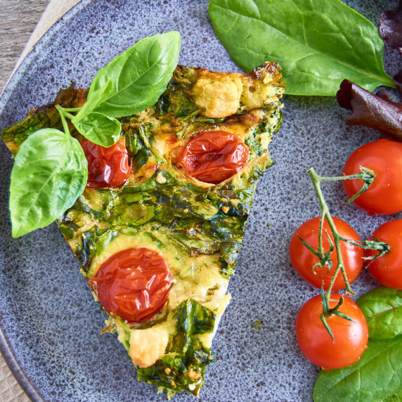 A piece of crustless spinach feta quiche topped with cherry tomatoes and fresh basil on a plate